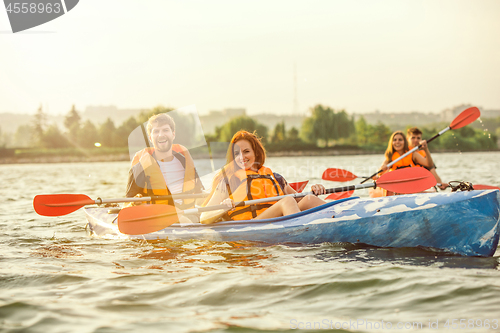 Image of Happy friends kayaking on river with sunset on the background