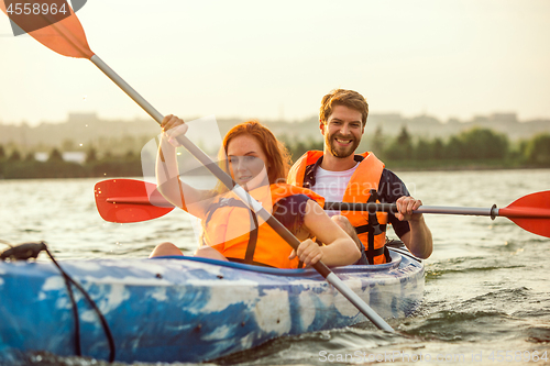 Image of Happy couple kayaking on river with sunset on the background