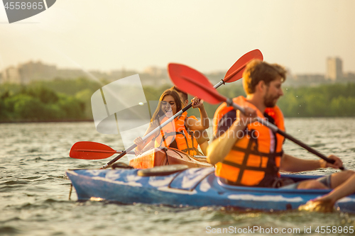 Image of Happy friends kayaking on river with sunset on the background