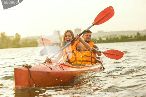 Image of Happy couple kayaking on river with sunset on the background