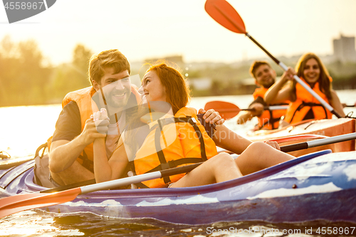 Image of Happy friends kayaking on river with sunset on the background