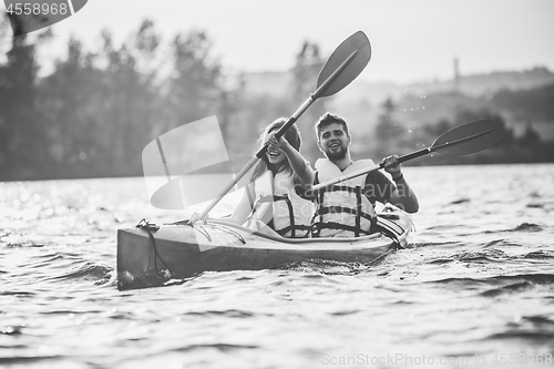 Image of Happy couple kayaking on river with sunset on the background