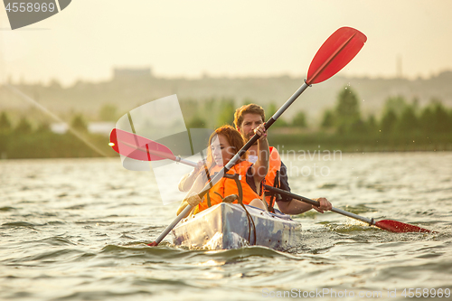 Image of Happy couple kayaking on river with sunset on the background