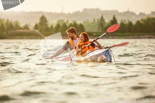 Image of Happy couple kayaking on river with sunset on the background