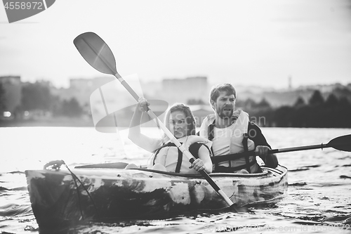 Image of Happy couple kayaking on river with sunset on the background