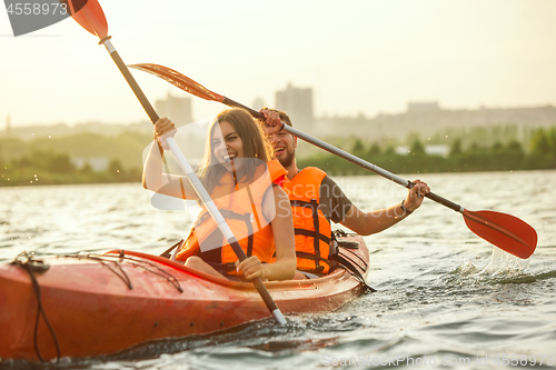 Image of Happy couple kayaking on river with sunset on the background