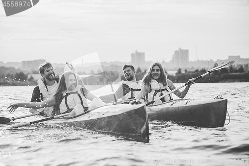 Image of Happy friends kayaking on river with sunset on the background