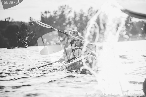 Image of Happy couple kayaking on river with sunset on the background