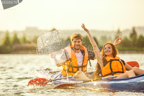 Image of Happy couple kayaking on river with sunset on the background