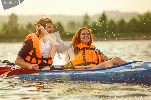 Image of Happy couple kayaking on river with sunset on the background