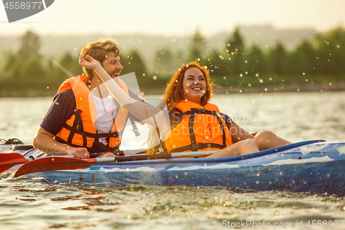 Image of Happy couple kayaking on river with sunset on the background