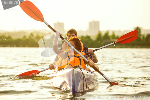 Image of Happy couple kayaking on river with sunset on the background