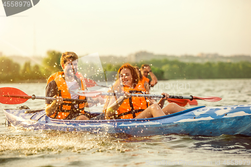 Image of Happy friends kayaking on river with sunset on the background