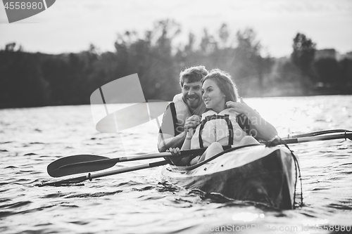 Image of Happy couple kayaking on river with sunset on the background