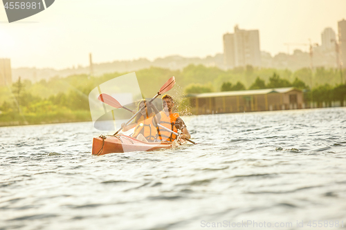 Image of Happy couple kayaking on river with sunset on the background