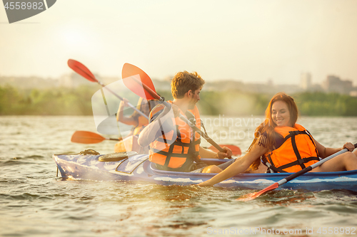 Image of Happy friends kayaking on river with sunset on the background