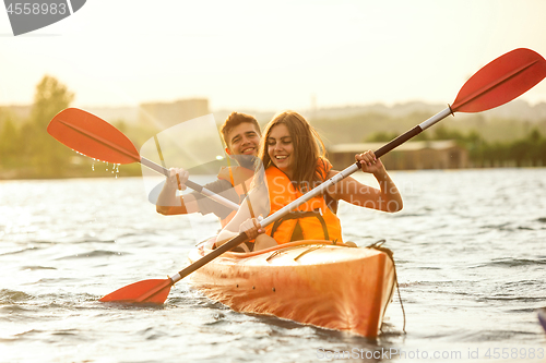 Image of Happy couple kayaking on river with sunset on the background