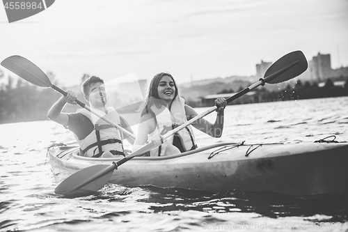 Image of Happy couple kayaking on river with sunset on the background