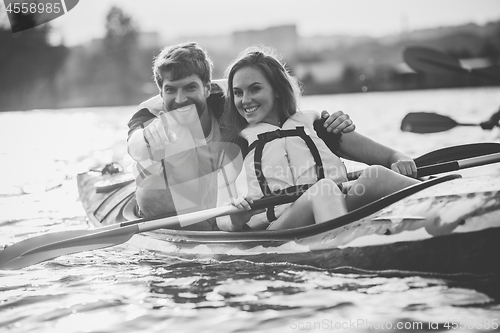 Image of Happy couple kayaking on river with sunset on the background