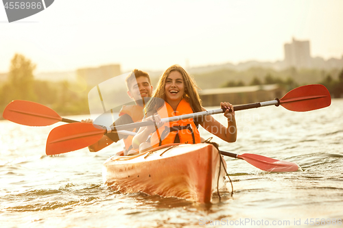 Image of Happy couple kayaking on river with sunset on the background