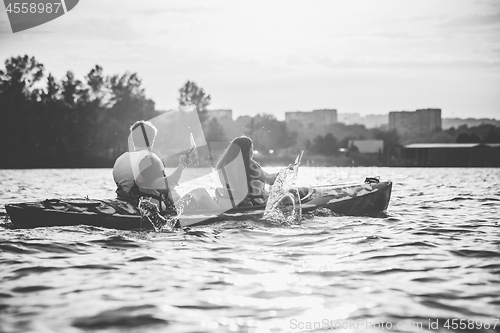 Image of Happy couple kayaking on river with sunset on the background