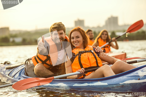 Image of Happy friends kayaking on river with sunset on the background