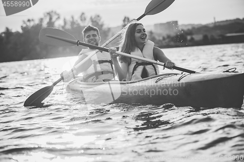 Image of Happy couple kayaking on river with sunset on the background