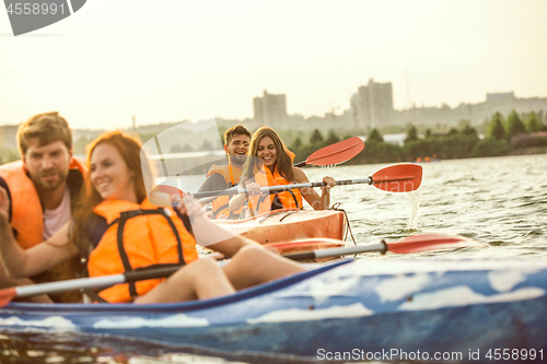 Image of Happy friends kayaking on river with sunset on the background