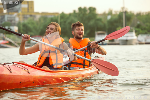 Image of Happy couple kayaking on river with sunset on the background