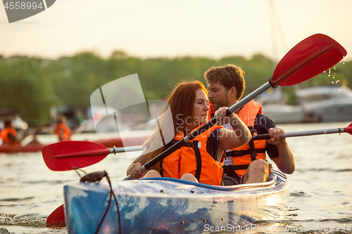 Image of Happy couple kayaking on river with sunset on the background