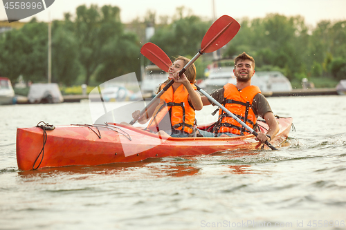 Image of Happy couple kayaking on river with sunset on the background