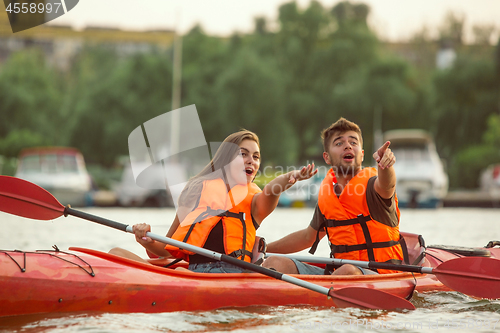 Image of Happy couple kayaking on river with sunset on the background