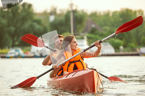 Image of Happy couple kayaking on river with sunset on the background