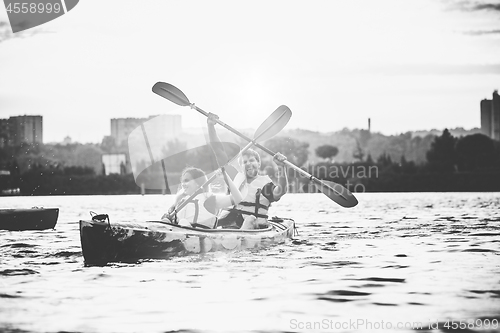 Image of Happy couple kayaking on river with sunset on the background