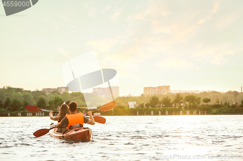 Image of Happy couple kayaking on river with sunset on the background