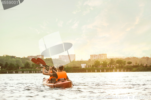 Image of Happy couple kayaking on river with sunset on the background