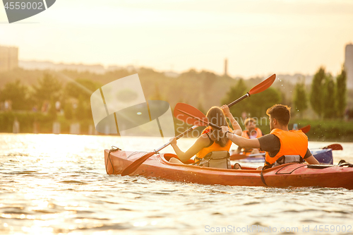 Image of Happy couple kayaking on river with sunset on the background