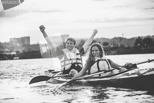 Image of Happy couple kayaking on river with sunset on the background