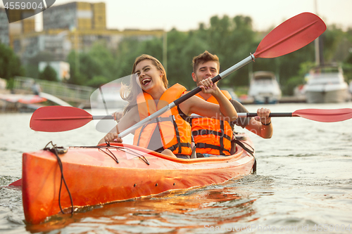 Image of Happy couple kayaking on river with sunset on the background