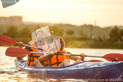 Image of Happy couple kayaking on river with sunset on the background