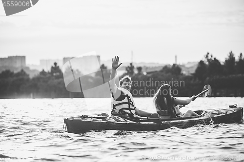 Image of Happy couple kayaking on river with sunset on the background