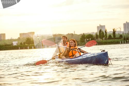 Image of Happy couple kayaking on river with sunset on the background