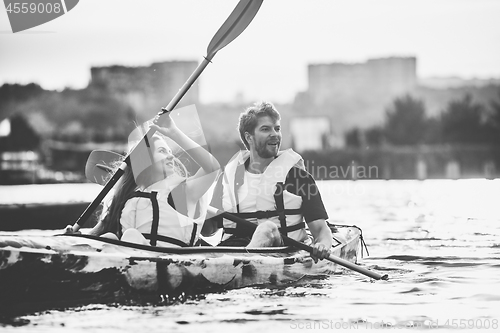 Image of Happy couple kayaking on river with sunset on the background