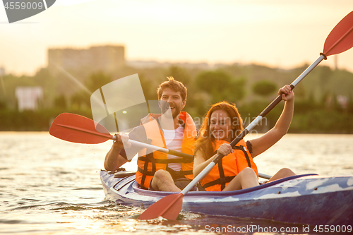 Image of Happy couple kayaking on river with sunset on the background