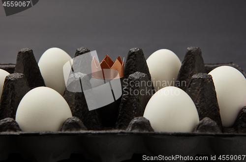 Image of White and painted black egg decorated with a paper gold crown in a black cardboard box on a black background with space for text. Wealth concept