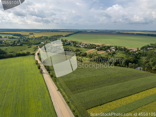 Image of Aerial view from a bird\'s-eye view to a rural landscape with a village, dirt road and agricultural fields of planted crops.