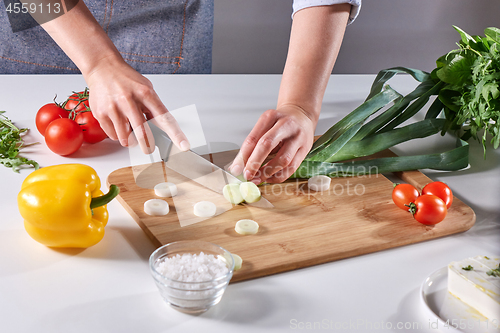 Image of Fresh leek slices cut into the hands of a female cook on a wooden board on the kitchen table around a variety of organic vegetables. Cooking Healthy Salad