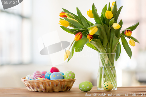 Image of colored easter eggs in basket and flowers at home