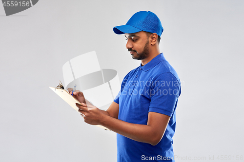 Image of happy indian delivery man with clipboard in blue