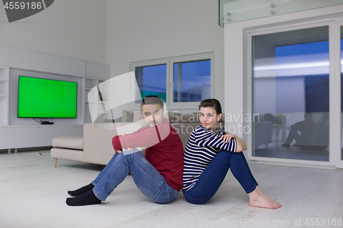 Image of young couple sitting with back to each other on floor